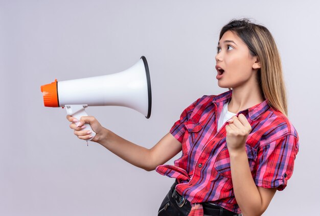 Una donna abbastanza giovane sorpresa in camicia controllata che tiene il megafono