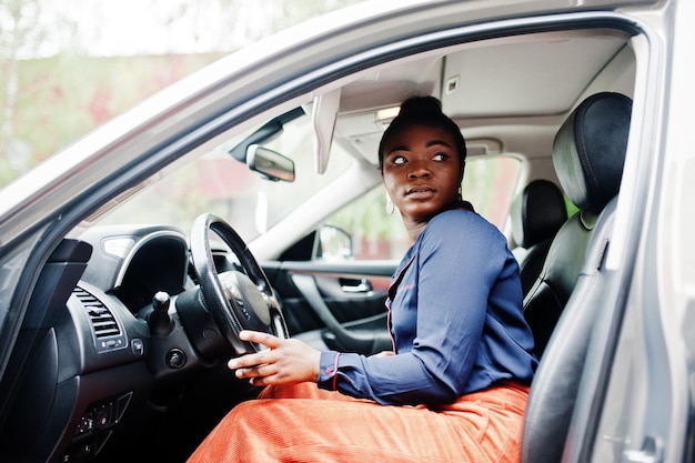 Una donna africana ricca di affari si siede sul sedile del conducente in un'auto suv d'argento con la porta aperta