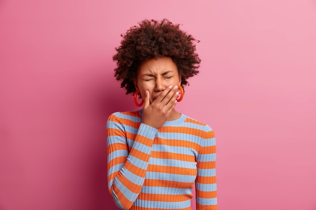 Una donna afroamericana addolorata e dispiaciuta copre gli occhi, piange per la disperazione, ha un'espressione del viso frustrata, indossa un maglione a righe casual, ha un grosso problema, è depressa per qualcosa. Burnout emotivo