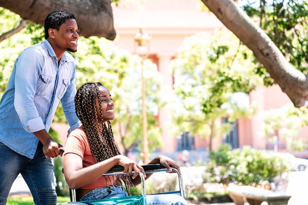 Una donna afroamericana su una sedia a rotelle si gode una passeggiata al parco con il suo ragazzo.