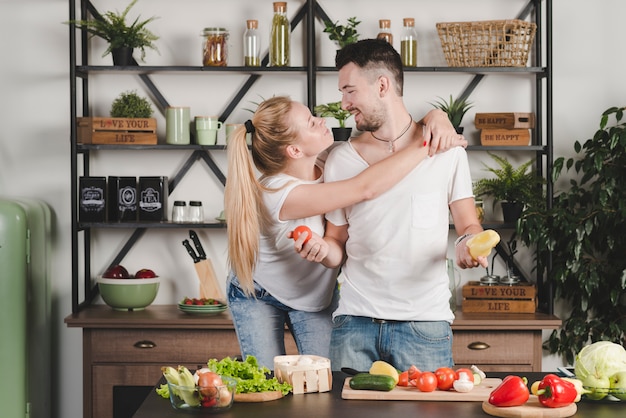 Una donna attraente che abbraccia il suo fidanzato tenendo le verdure in cucina