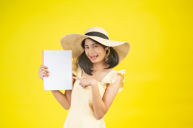 Una donna bella e felice che indossa un grande cappello e in possesso di un libro bianco su un giallo.