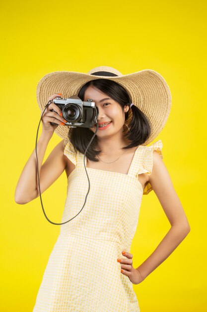 Una donna bella e felice che indossa un grande cappello e una macchina fotografica su un giallo.