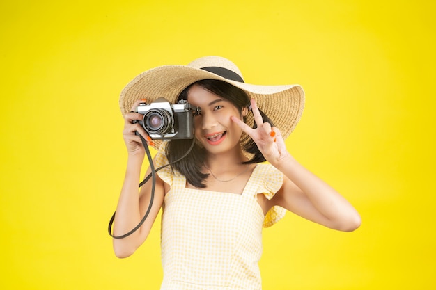 Una donna bella e felice che indossa un grande cappello e una macchina fotografica su un giallo.