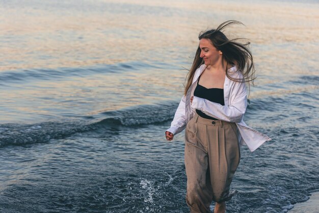 Una donna cammina lungo il mare a piedi nudi allo spazio della copia del tramonto