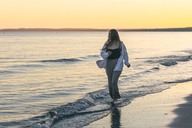 Una donna cammina lungo il mare a piedi nudi allo spazio della copia del tramonto