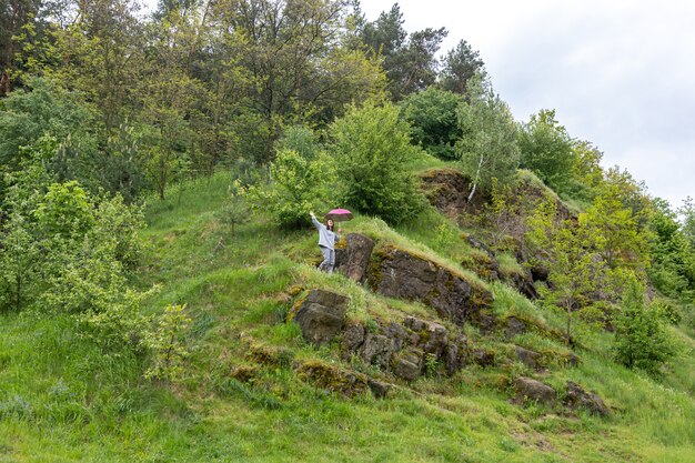 Una donna cammina sotto un ombrellone in montagna, tra le rocce ricoperte di verde