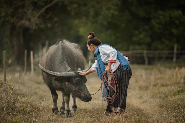 Una donna cammina tenendo una corda di bufalo nel prato.