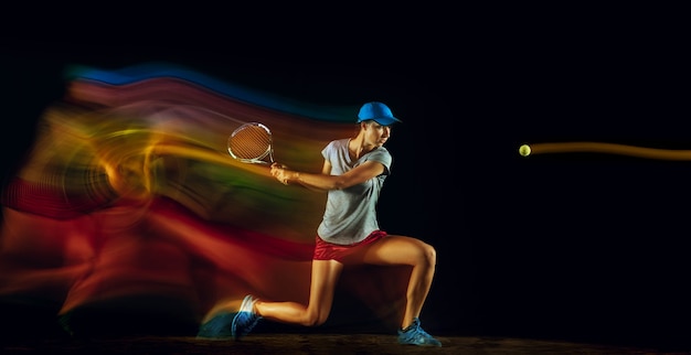Una donna che gioca a tennis isolata sul muro nero in luce mista e stobe