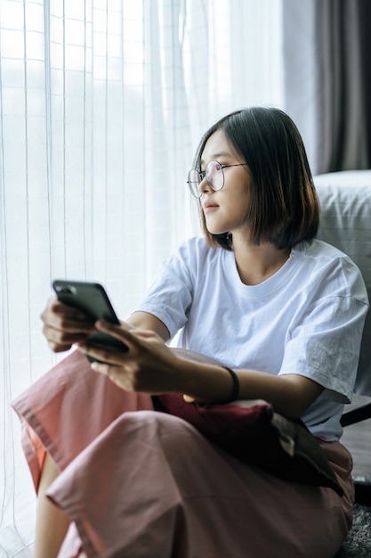 Una donna che indossa una camicia bianca, seduta sul letto e giocando uno smartphone.