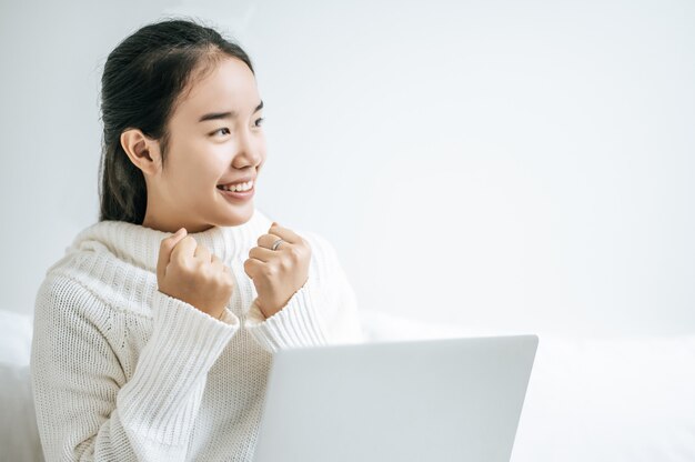 Una donna che indossa una camicia bianca sul letto e gioca felicemente al computer portatile.