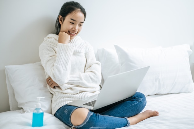 Una donna che indossa una camicia bianca sul letto e gioca felicemente al computer portatile.