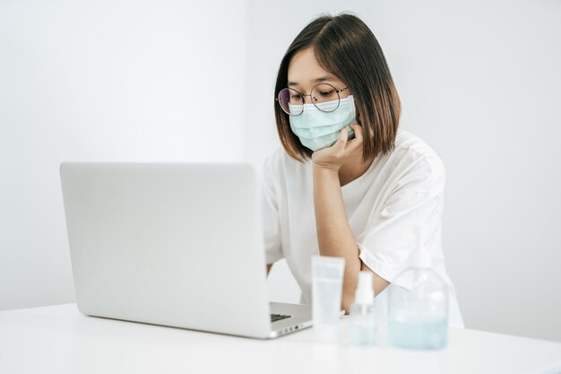 Una donna che indossa una maschera giocando un computer portatile e avendo una bottiglia di gel lavamani.