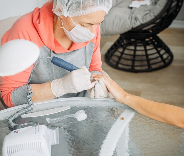 Una donna che riceve manicure da una donna in guanti e maschera nel salone di bellezza durante il giorno