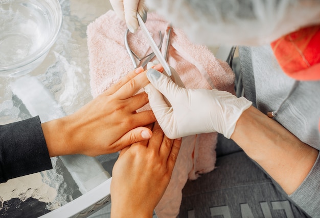 Una donna che riceve manicure da una donna in guanti e maschera nel salone di bellezza durante il giorno