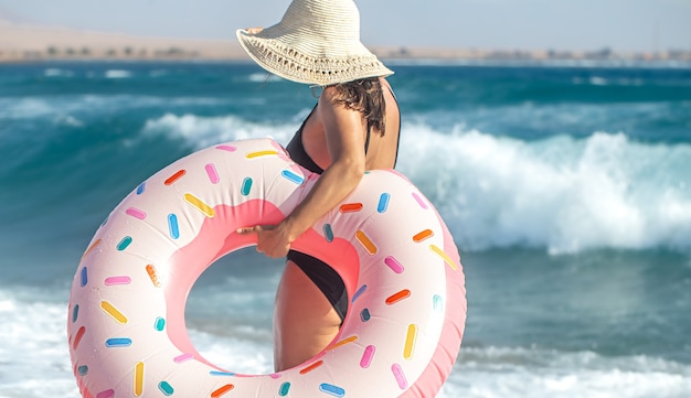 Una donna con un cappello con un cerchio da nuoto a forma di ciambella in riva al mare. Il concetto di svago e intrattenimento in vacanza.