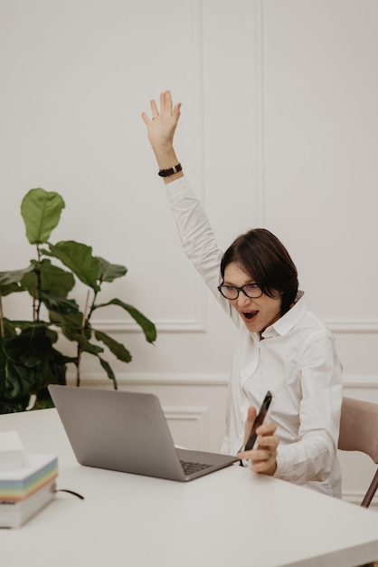 Una donna d'affari caucasica di successo con gli occhiali guarda lo schermo del laptop gioendo per le buone notizie che leggeva mentre era seduta al tavolo