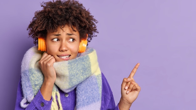 Una donna dall'aspetto piacevole e preoccupato con i capelli scuri e crespi guarda nervosamente e indica lo spazio della copia, ascolta la traccia audio in cuffia.