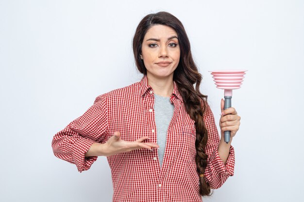 Una donna delle pulizie caucasica seria che tiene in mano e indica lo stantuffo di gomma