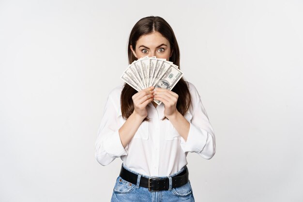 Una donna entusiasta che mostra denaro contante e sorridente ha ottenuto un micro credito in prestito in piedi felice contro w ...