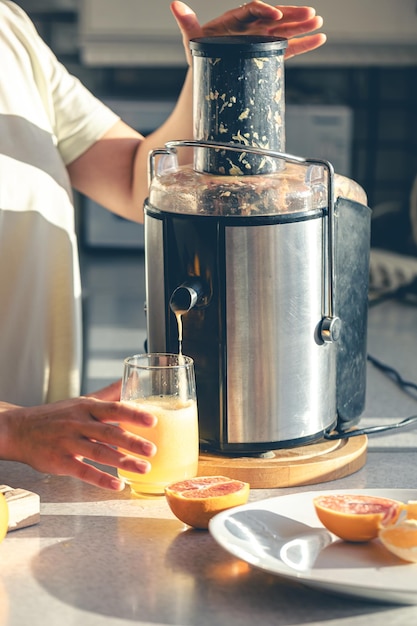 Una donna fa succo d'arancia a casa in cucina con uno spremiagrumi elettrico