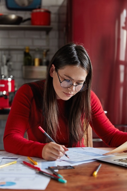 Una donna impegnata pensa al target o alla società di pianificazione, fa statistiche o ricerche analitiche, si siede al desktop, all'interno della cucina