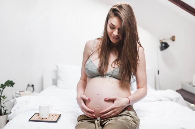 Una donna incinta che si siede sul letto che tiene la sua pancia con due mani