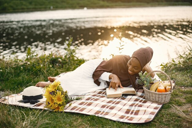 Una donna musulmana giaceva sulla coperta da picnic scozzese vicino al fiume e leggeva un libro