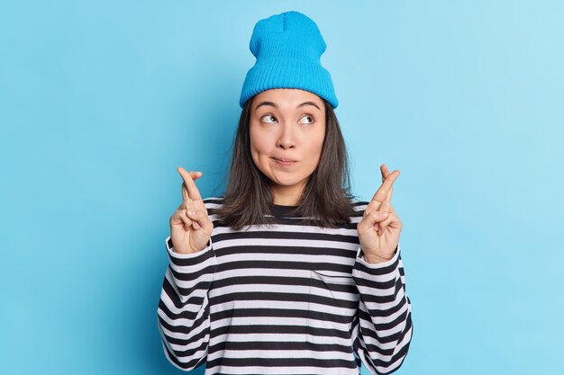 Una donna pensosa e concentrata con i capelli scuri tiene le dita incrociate, crede nella buona sorte, speranze di fortuna, brama di desideri che si avverano