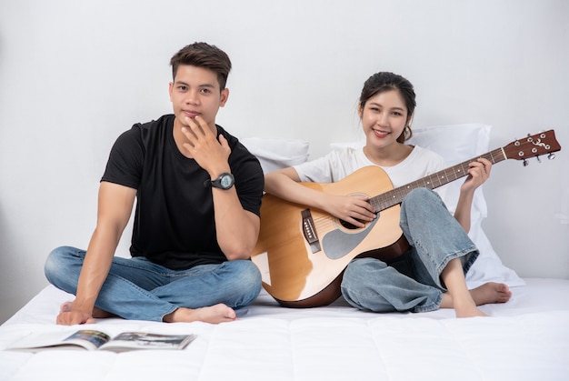 Una donna seduta suona la chitarra e un uomo tiene un libro e canta.