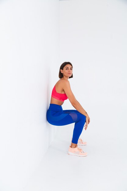 Una donna sportiva abbronzata in forma con addominali, curve fitness, che indossa top e leggings blu su bianco fa esercizio sulla sedia