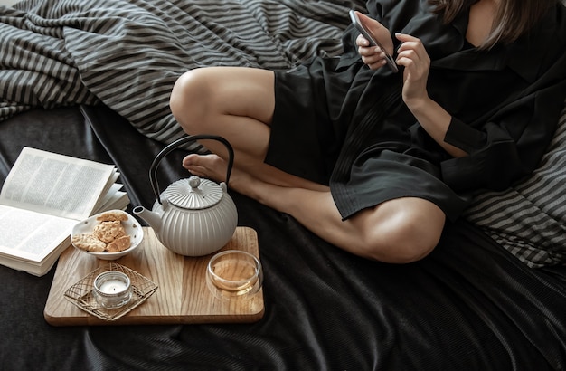 Una donna sta facendo colazione con tè e biscotti, sdraiata a letto in un giorno libero.