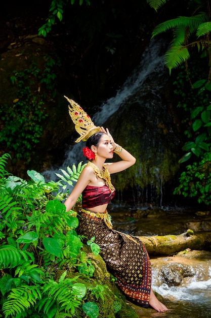 Una donna vestita con un abito thailandese antico presso la cascata.