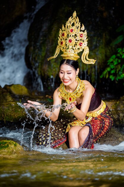 Una donna vestita con un abito thailandese antico presso la cascata.