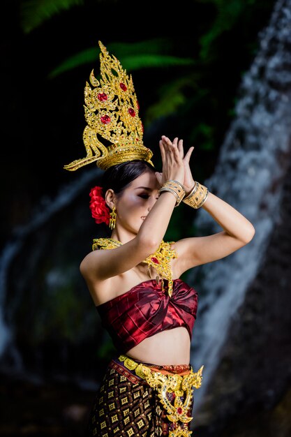 Una donna vestita con un abito thailandese antico presso la cascata.