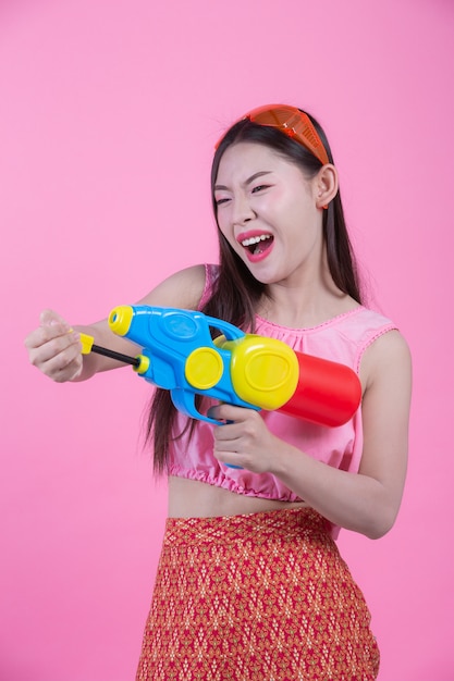 Una donna vestita in abiti tradizionali tailandesi tradizionali tenendo una pistola ad acqua su uno sfondo rosa.