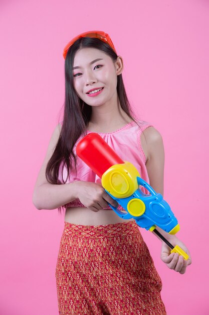 Una donna vestita in abiti tradizionali tailandesi tradizionali tenendo una pistola ad acqua su uno sfondo rosa.