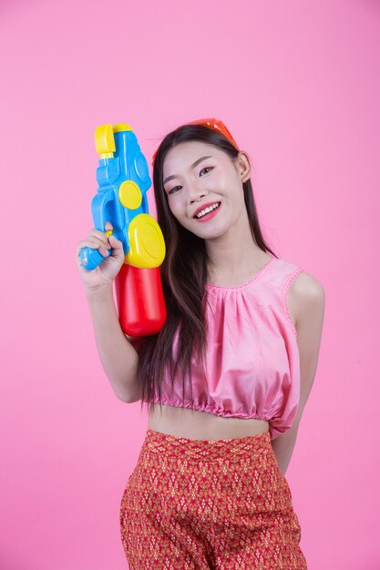 Una donna vestita in abiti tradizionali tailandesi tradizionali tenendo una pistola ad acqua su uno sfondo rosa.