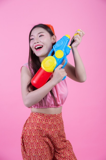 Una donna vestita in abiti tradizionali tailandesi tradizionali tenendo una pistola ad acqua su uno sfondo rosa.