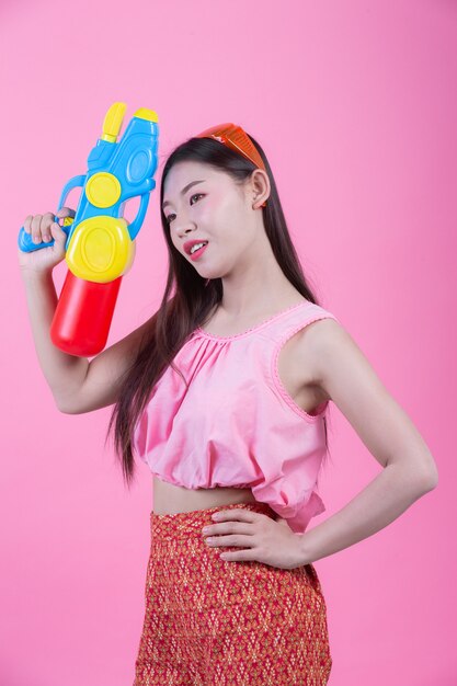 Una donna vestita in abiti tradizionali tailandesi tradizionali tenendo una pistola ad acqua su uno sfondo rosa.