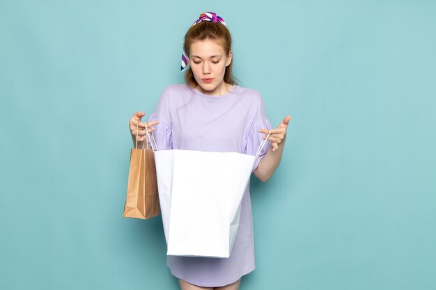 Una femmina attraente di vista frontale in camicia-vestito blu che tiene i pacchetti della spesa sull'azzurro