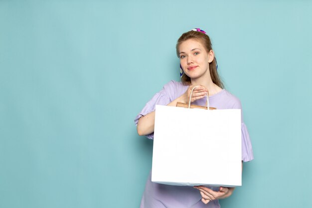 Una femmina attraente di vista frontale in camicia-vestito blu che tiene pacchetto di acquisto bianco sull'azzurro