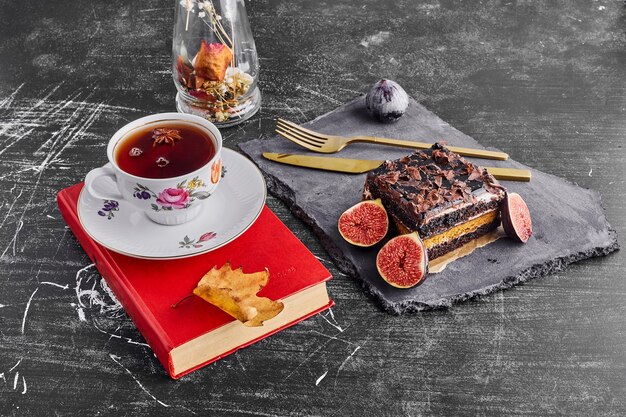 Una fetta di torta al cioccolato con frutta e una tazza di tè su un piatto di pietra.