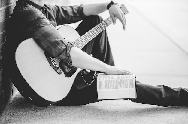 Una foto in scala di grigi di un maschio con una chitarra e una Bibbia aperta