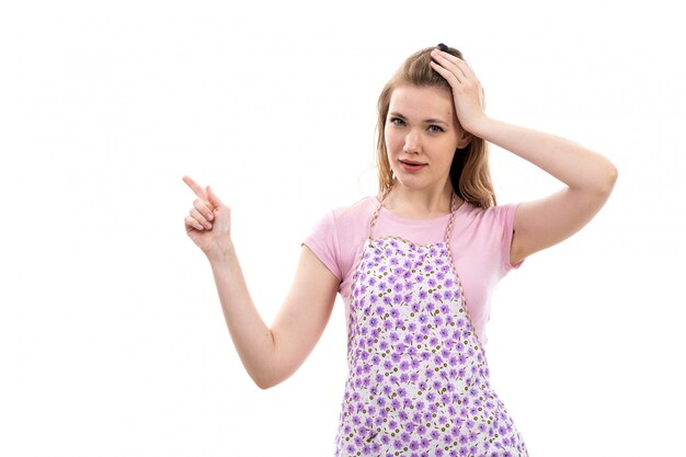 Una giovane bella casalinga di vista frontale in mantello variopinto della camicia rosa che giudica preoccupata la sua testa che pensa