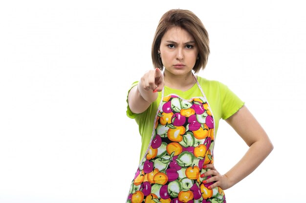 Una giovane bella casalinga di vista frontale nell'espressione arrabbiata del capo variopinto della camicia verde sulla cucina bianca della femmina della casa del fondo