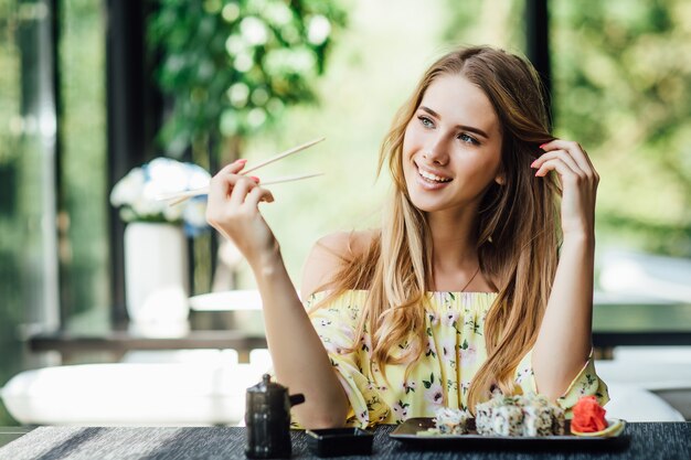 Una giovane bella donna bionda e carina che mangia sushi sulla terrazza estiva di un ristorante giapponese