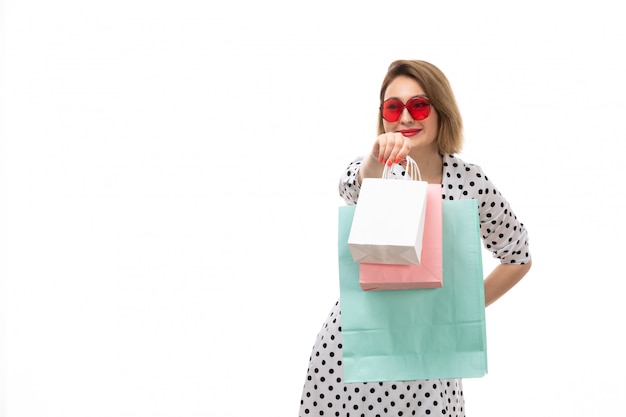 Una giovane bella donna di vista frontale in vestito a pois in bianco e nero in occhiali da sole rossi che tengono posa dei pacchetti di acquisto
