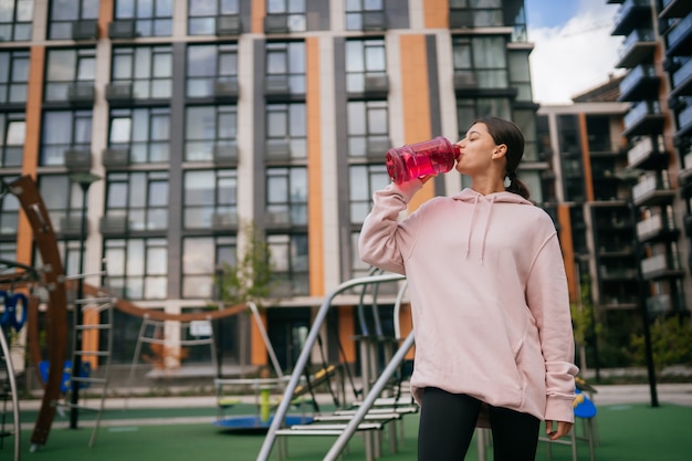 Una giovane bella donna sta bevendo acqua nel parco giochi