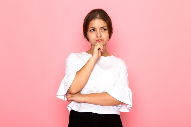 Una giovane bella femmina di vista frontale in camicia bianca che posa con l'espressione di pensiero